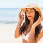 Closeup Of Smiling Beautiful Young Woman At Beach With Straw Hat