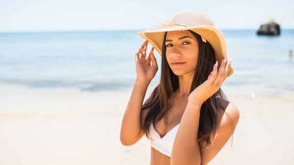 Closeup Of Smiling Beautiful Young Woman At Beach With Straw Hat